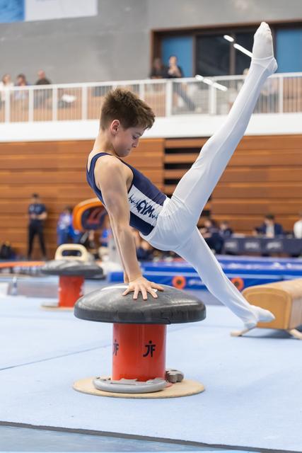 Young gymnast demonstrates a V-sit position on the pommel horse, displaying strength and control in a gym competition setting