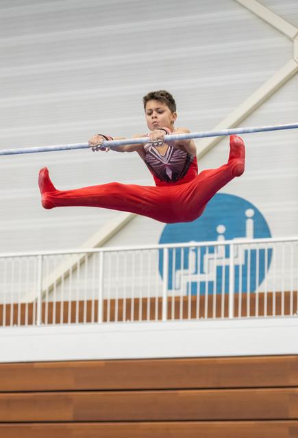 Gymnast performing horizontal bar routine with legs extended horizontally, displaying intense focus and control mid-air