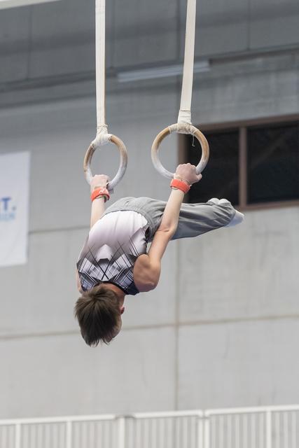 Young gymnast performing an inverted hang position on rings in an indoor training facility