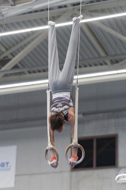 Young gymnast performing an inverted hang on rings in an indoor training facility, demonstrating strength and control