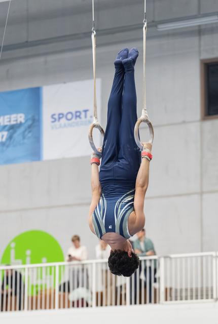Male gymnast performing an inverted hang position on gymnastics rings during training session in indoor sports hall