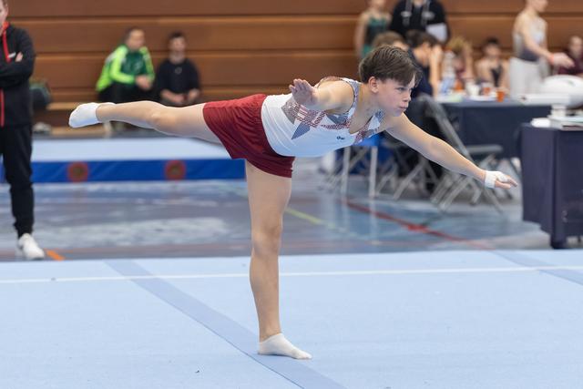 Young gymnast executes an arabesque balance on floor mat, demonstrating control and extension during routine