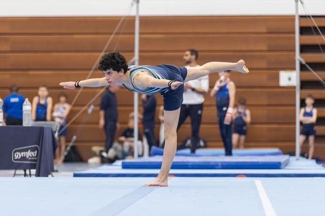 Gymnast executes a graceful arabesque balance on floor, arms extended, demonstrating flexibility and control during routine