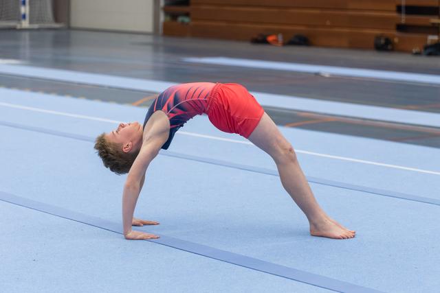 Young gymnast executing a deep backbend bridge on training floor, demonstrating remarkable flexibility and control