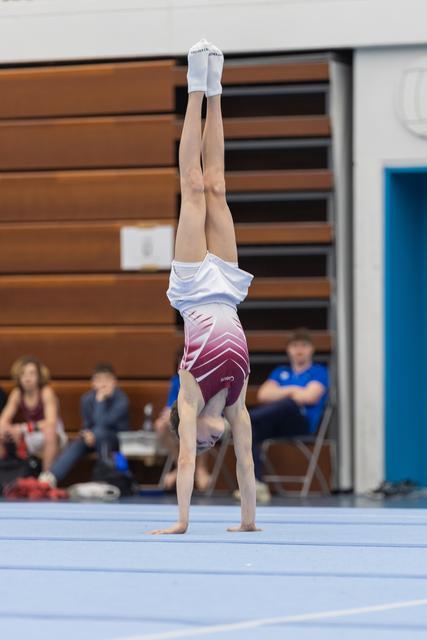 Gymnast performs a vertical handstand on floor exercise, demonstrating balance and control during routine at indoor competition