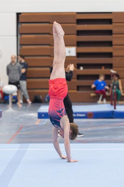 Young gymnast performs a straight handstand on floor exercise mat during training session in gymnasium