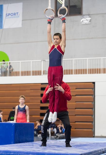 Gymnast holds a handstand position on rings while a coach spots from below in an indoor training facility