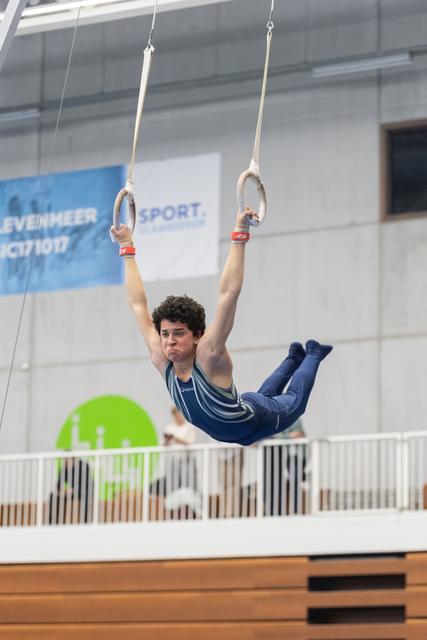 Male gymnast demonstrates strength hold on rings apparatus during training, body horizontal with legs extended forward