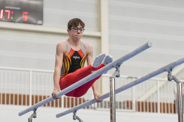 Young gymnast in colorful leotard demonstrates parallel bars routine with concentrated expression and extended form