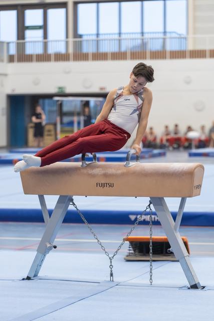 Male gymnast executing a horizontal hold on pommel horse, demonstrating strength and focus during routine at indoor facility
