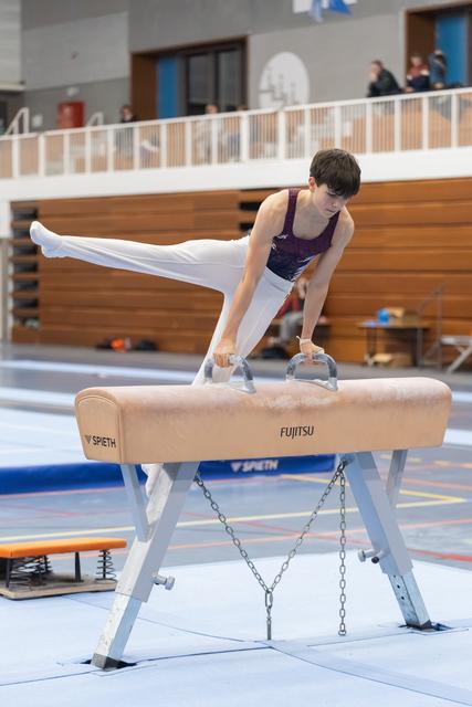 Young gymnast executes a scissor move on pommel horse, legs extended horizontally in focused concentration at training facility