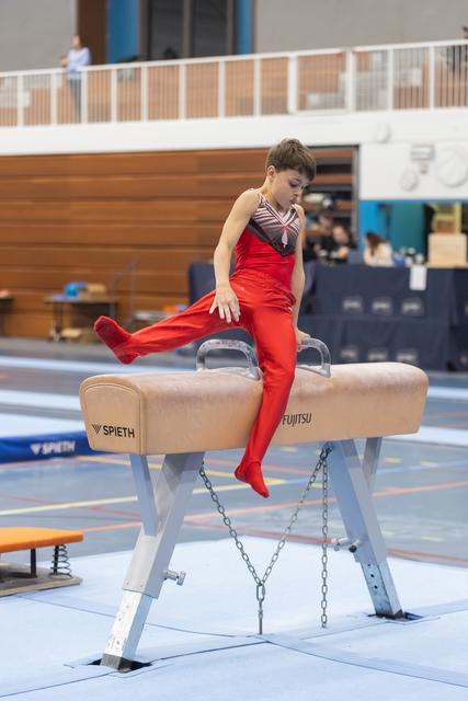 Young gymnast in red outfit executing a side support position on the pommel horse during training session