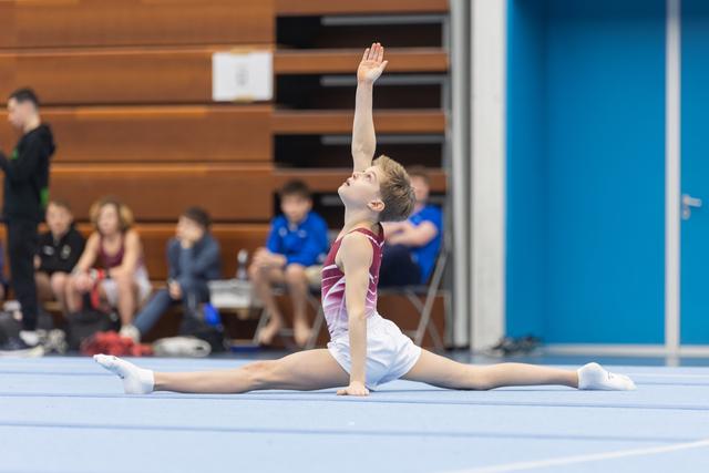 Young gymnast executes a full split on floor with one arm raised gracefully, showcasing flexibility during routine performance