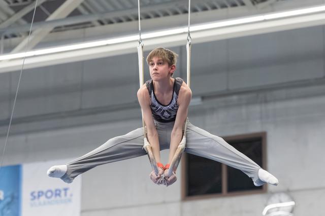 Young gymnast performing a straddle position on still rings, displaying intense concentration and control in the training facility