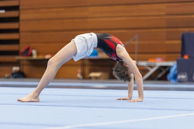 Young gymnast executing a backbend bridge position during floor exercise practice in an indoor training facility