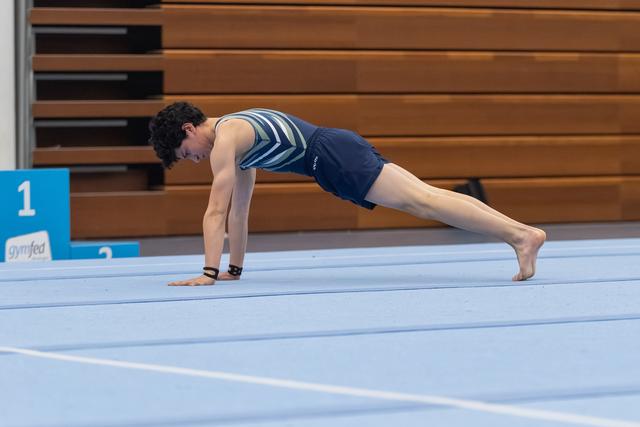 Male gymnast holds a plank position on a blue gymnastics mat, demonstrating strength and control in a gym setting