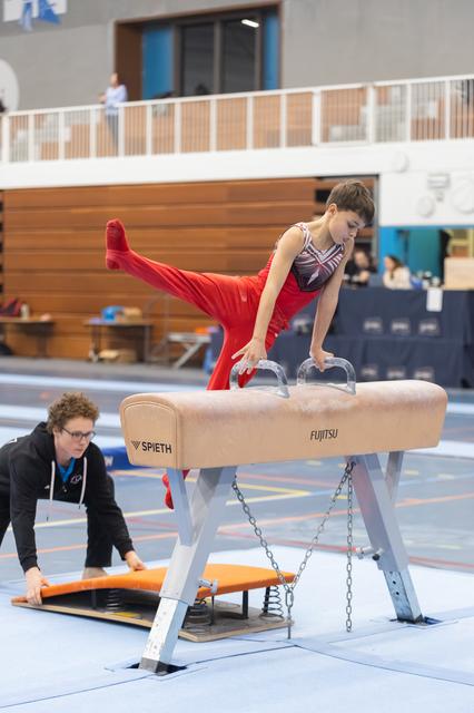 Gymnast performs horizontal hold on pommel horse with extended legs while coach observes during training session