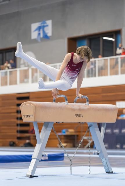 Gymnast performs impressive straddle hold on pommel horse, legs extended horizontally while balancing on handles in training facility