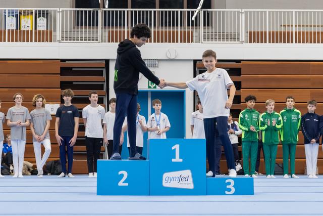 Coach presenting medal to smiling young gymnast in white standing on first place podium during awards ceremony