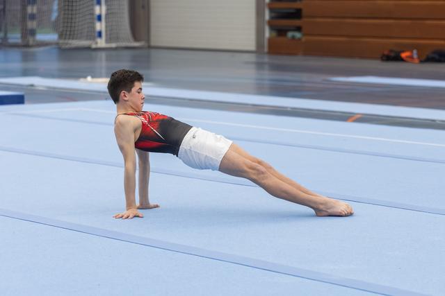 Male gymnast holds reverse plank position during floor training, demonstrating strength and body control in gymnasium