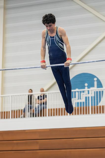 Young male gymnast performing on horizontal bar during routine, displaying focused concentration and athletic form