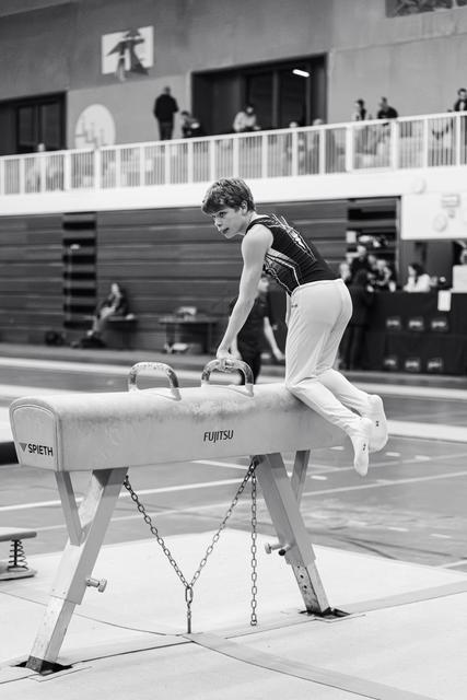 Male gymnast prepares for pommel horse routine, gripping handles with focused concentration in competition venue