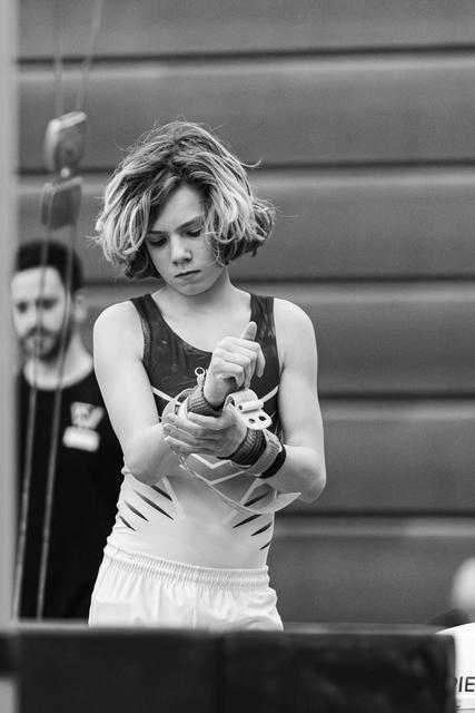 Young female gymnast with short blonde hair concentrates while applying chalk to her hands in preparation for her routine