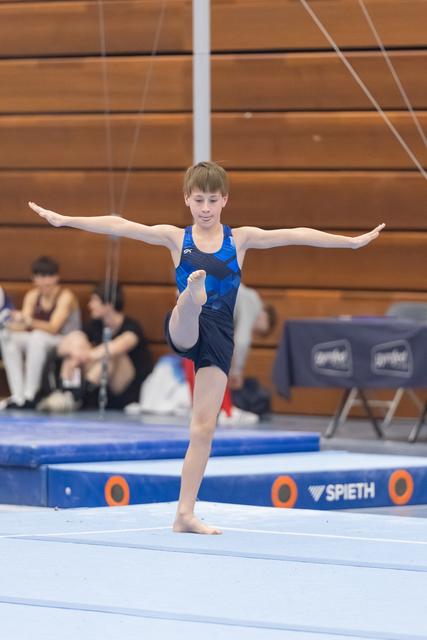 Young gymnast performing a standing balance pose with arms extended and one leg raised during floor exercise routine