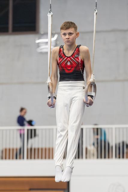 Young male gymnast performing on parallel bars, displaying intense concentration in white pants and red patterned leotard