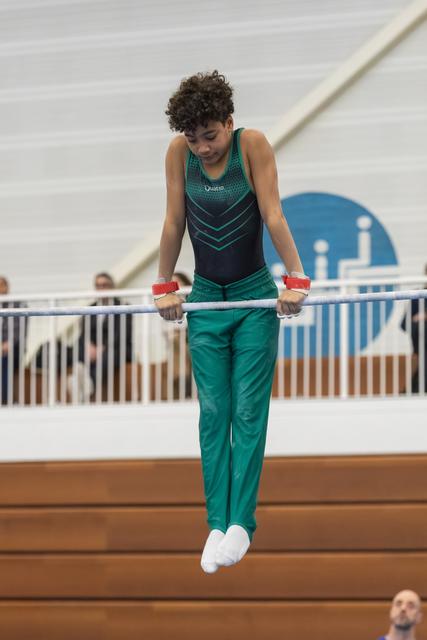 Young gymnast in teal leotard concentrating during uneven bars routine, gripping the bar with chalked hands