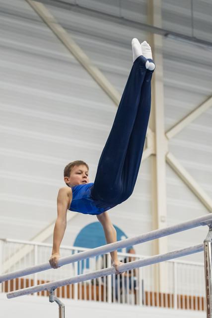 Young gymnast performs handstand on parallel bars with legs extended upward, demonstrating strength and form in training facility
