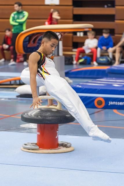 Young male gymnast performing a strength hold on mushroom circle apparatus, legs extended horizontally in competition venue