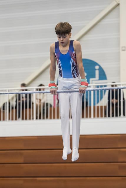 Young gymnast in blue leotard performing on parallel bars with intense concentration, white pants and hand grips visible