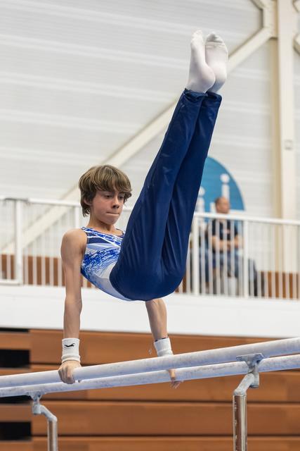Young gymnast performs an L-sit hold on parallel bars, legs extended upward, displaying strength and focus in training facility