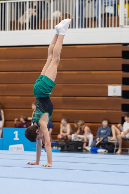 Young gymnast performs a straight handstand on floor exercise mat, demonstrating control and balance during routine