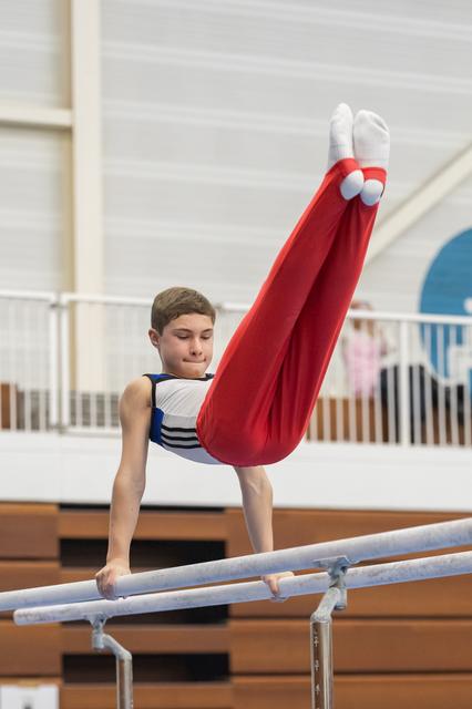Young male gymnast executing an L-sit hold on parallel bars, demonstrating strength and control in the training facility