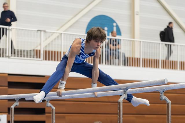 Young male gymnast in blue leotard performs on parallel bars, displaying strength and concentration during his routine