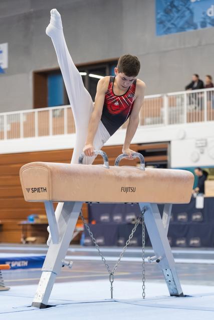 Male gymnast executing a straddle position on pommel horse, displaying strength and control during his routine
