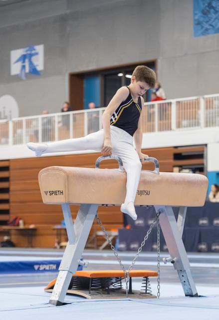 Young gymnast performing a scissor move on pommel horse, displaying concentration and form during his routine
