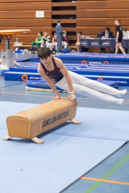 Young gymnast in maroon leotard executes a skill on the pommel horse, body extended horizontally during training session.