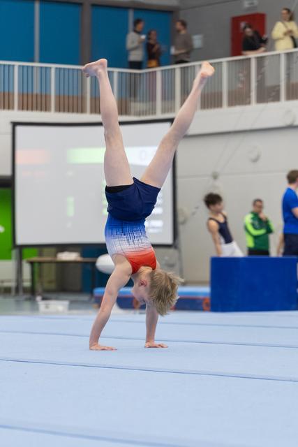 Young gymnast executes a controlled handstand during floor routine, legs extended vertically in competition setting