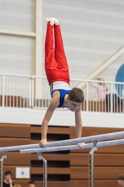 Young male gymnast executes a vertical handstand on parallel bars, legs pointed straight up, in an indoor training facility