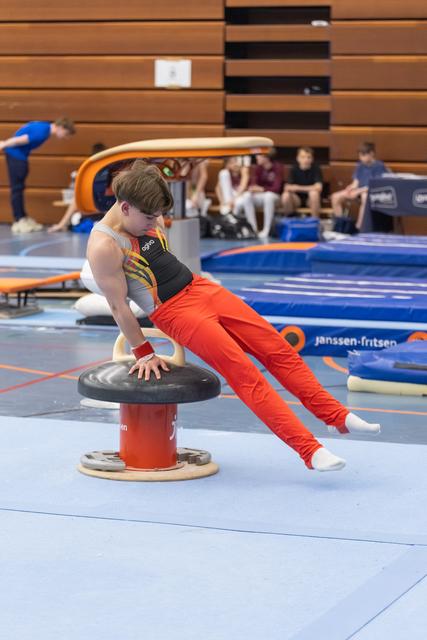 Young gymnast in red pants and black tank top performs a support hold on the mushroom apparatus during training