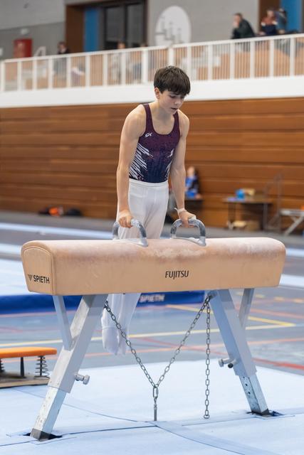 Young gymnast performing on pommel horse with intense concentration, gripping handles in indoor training facility