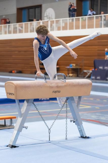 Young gymnast performs side position on pommel horse, leg extended high, white grips visible during training
