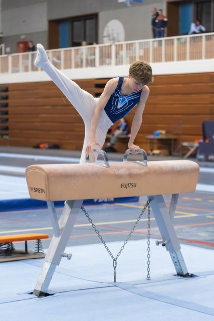 Young gymnast performs handstand with leg extension on pommel horse, demonstrating strength and balance in training facility