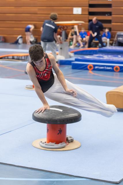 Young gymnast performs a circle drill on mushroom apparatus, extending his body horizontally during practice session
