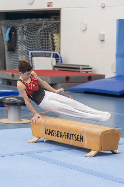 Young male gymnast performs a side support position on pommel horse during training in gymnasium