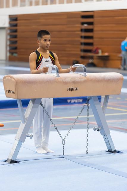 Young gymnast in white and yellow uniform positions hands on pommel horse grips, focused expression before routine