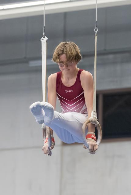 Young gymnast performs L-sit position on rings, concentrating intently with legs extended forward in training facility